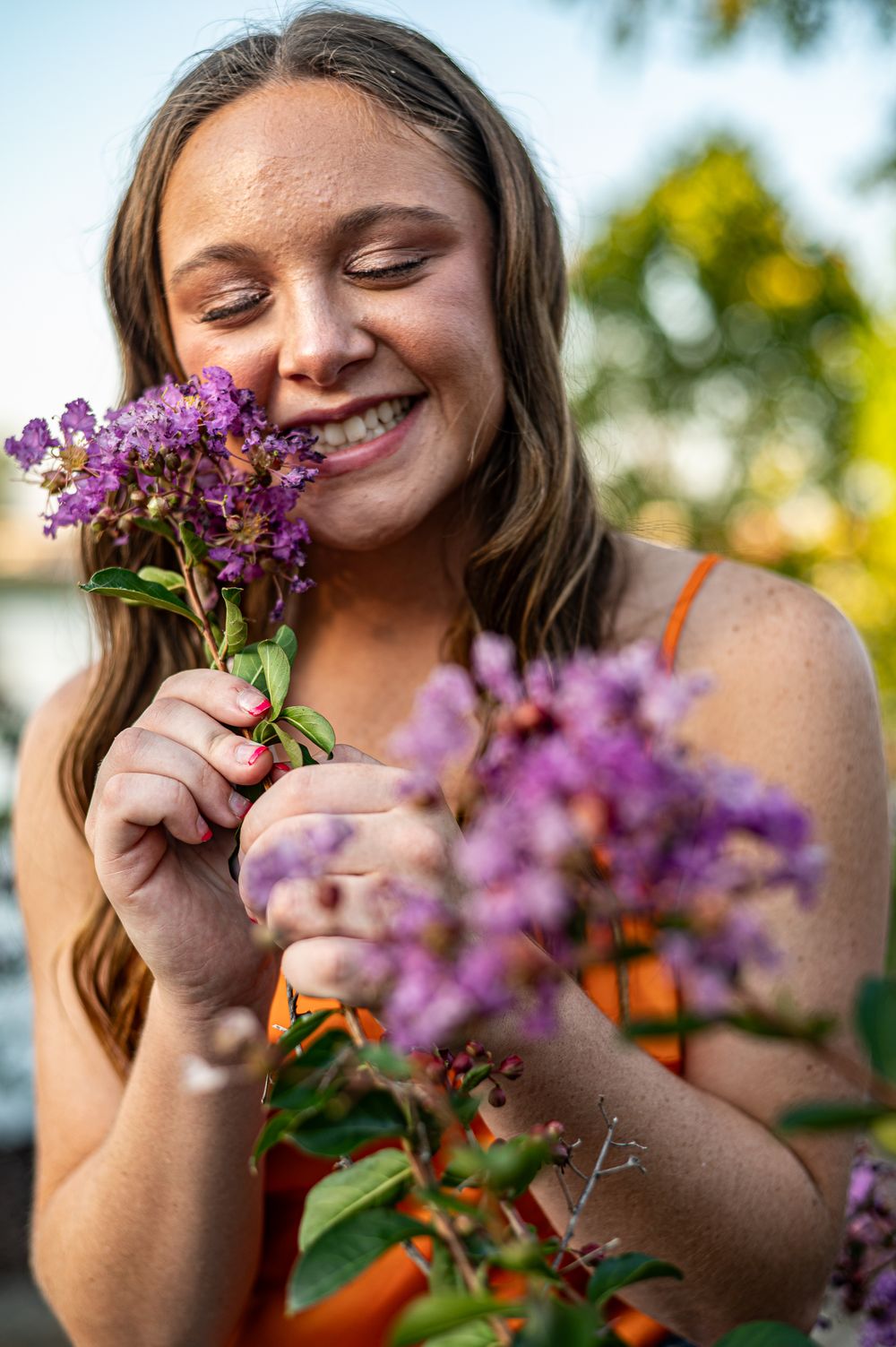 Young woman smiling with eyes closed while holding purple wildflowers outdoors in warm golden light.