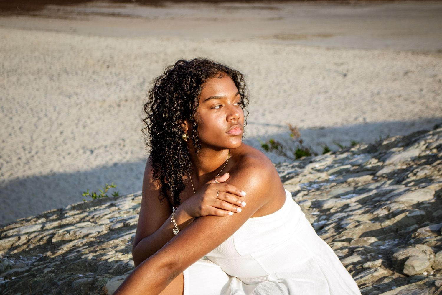 Person in white dress poses on beach during golden hour.