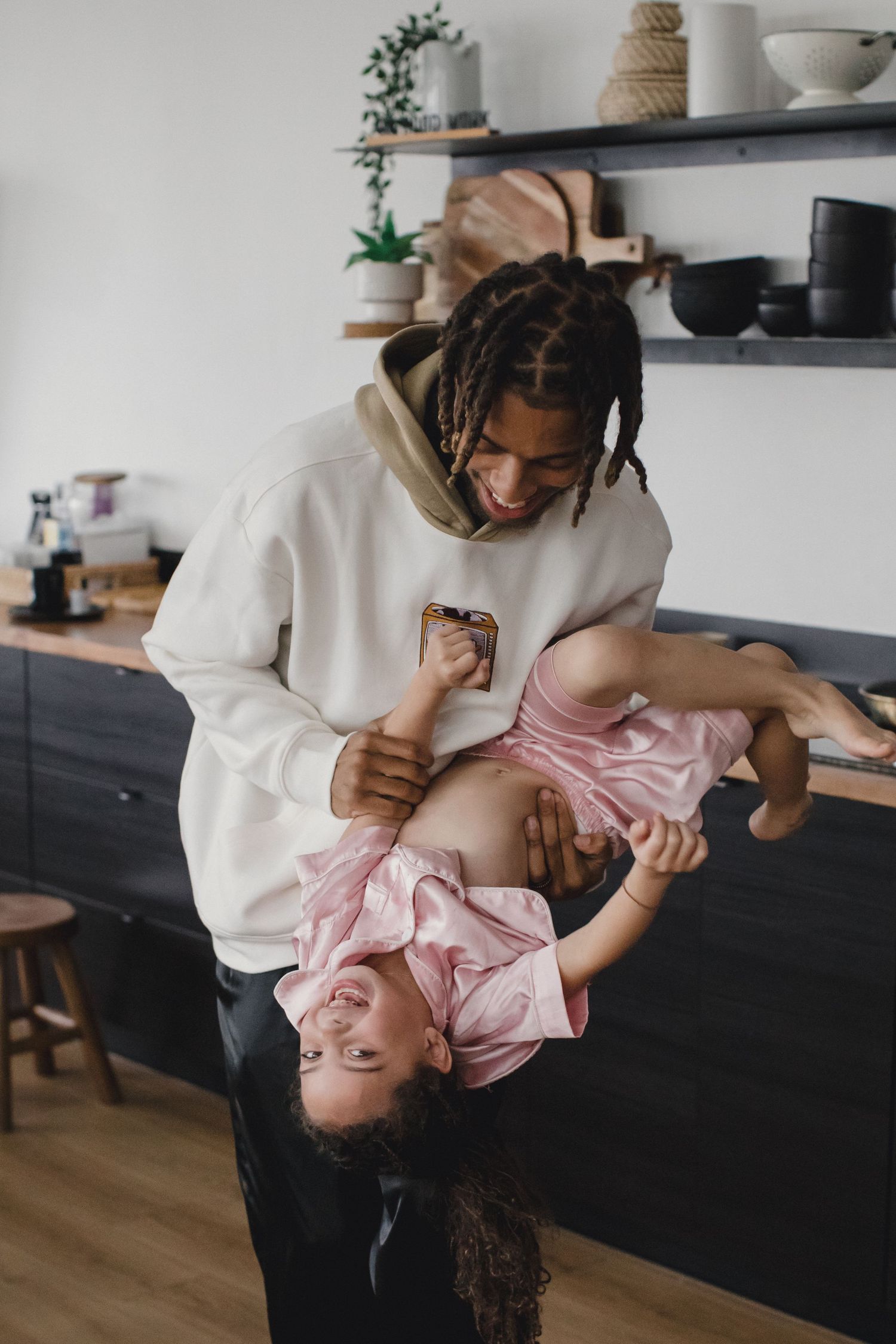 A playful moment in a modern kitchen as a parent holds a laughing child upside down.
