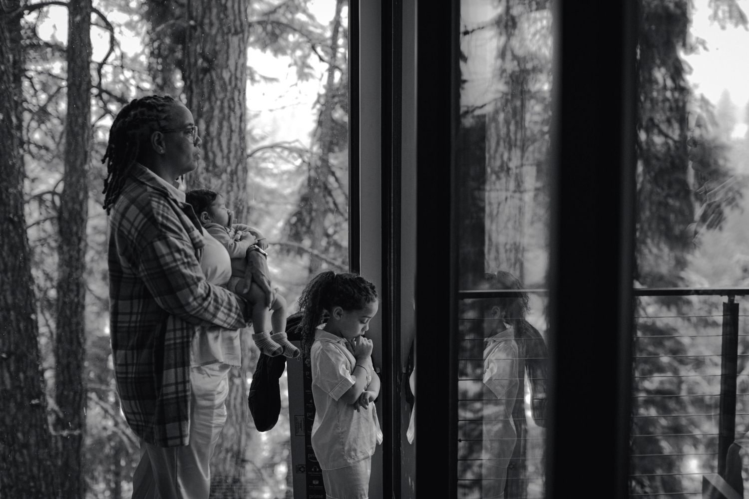 A black and white photo of people looking through large windows at a snowy forest view.