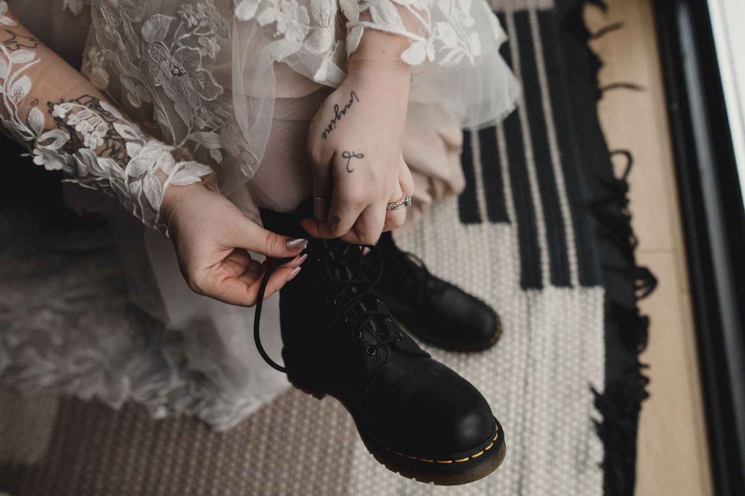 Close-up of hands tying black boots with delicate lace sleeves visible.