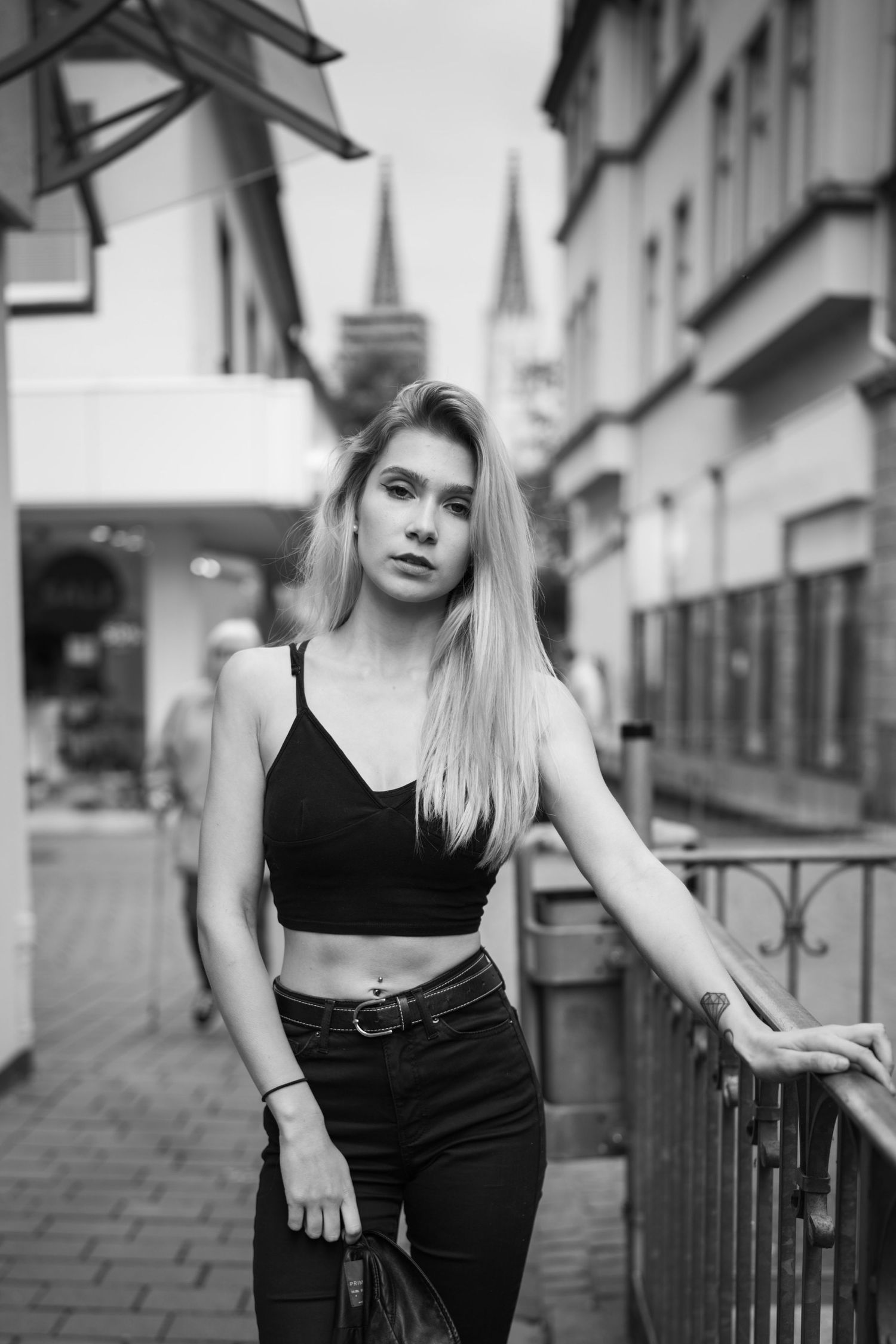 Schwarz-Weiß-Porträt einer Frau in bauchfreiem Top und Jeans, die auf einer europäischen Stadtstraße steht.