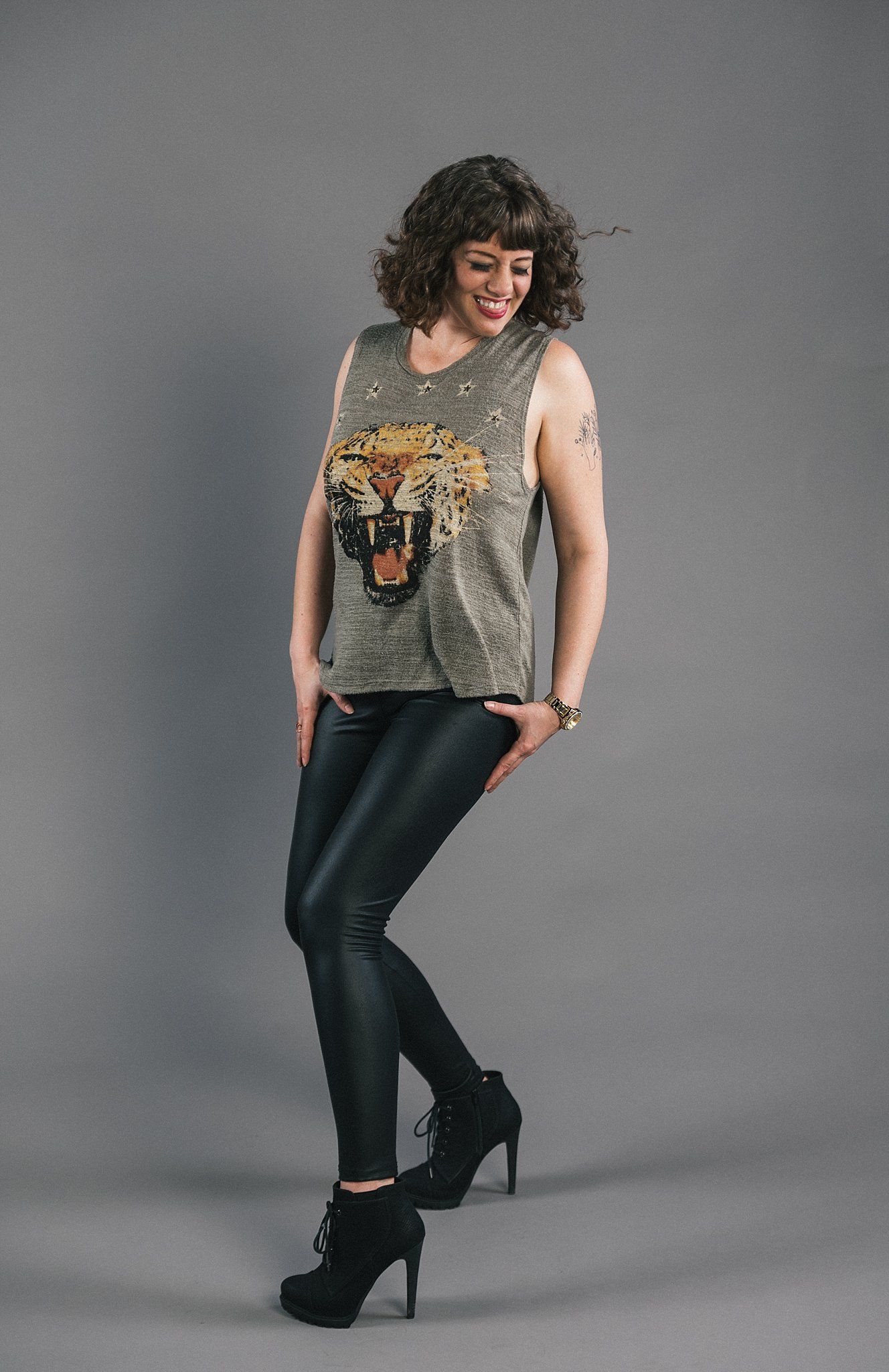 An edgy casual look featuring a graphic tank top and leather pants against a gray backdrop.