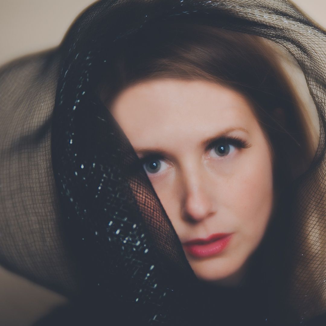 Artistic portrait through sheer black fabric creating dramatic lighting effect.