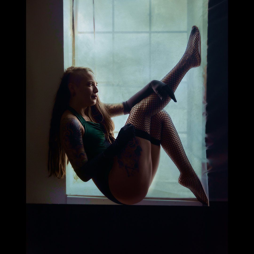 Artistic window silhouette of someone wearing fishnet stockings in a dramatic pose.