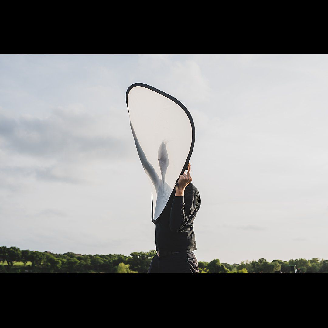 Person in black clothing swinging a large rope against a cloudy sky.