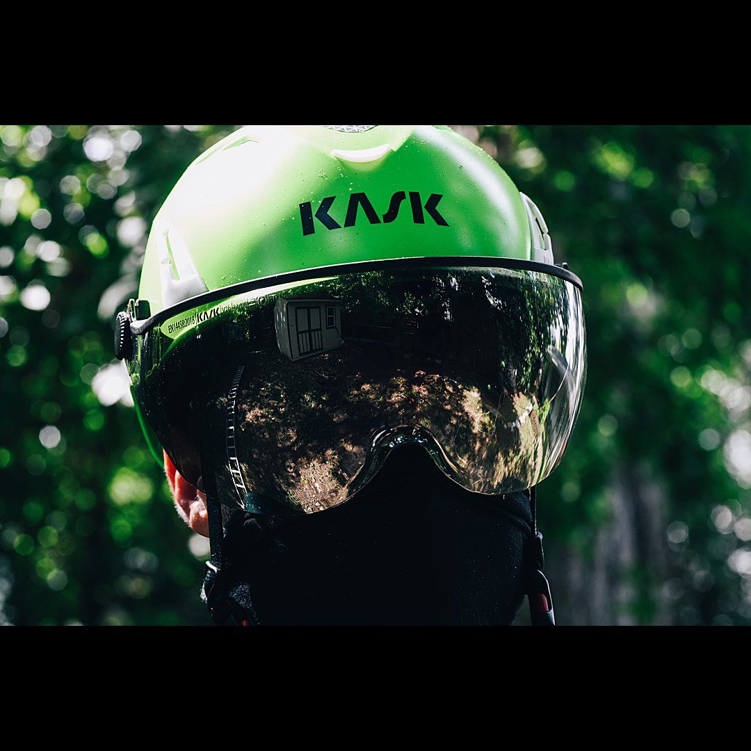 Close-up of a green Kask cycling helmet with reflective visor against bokeh background.