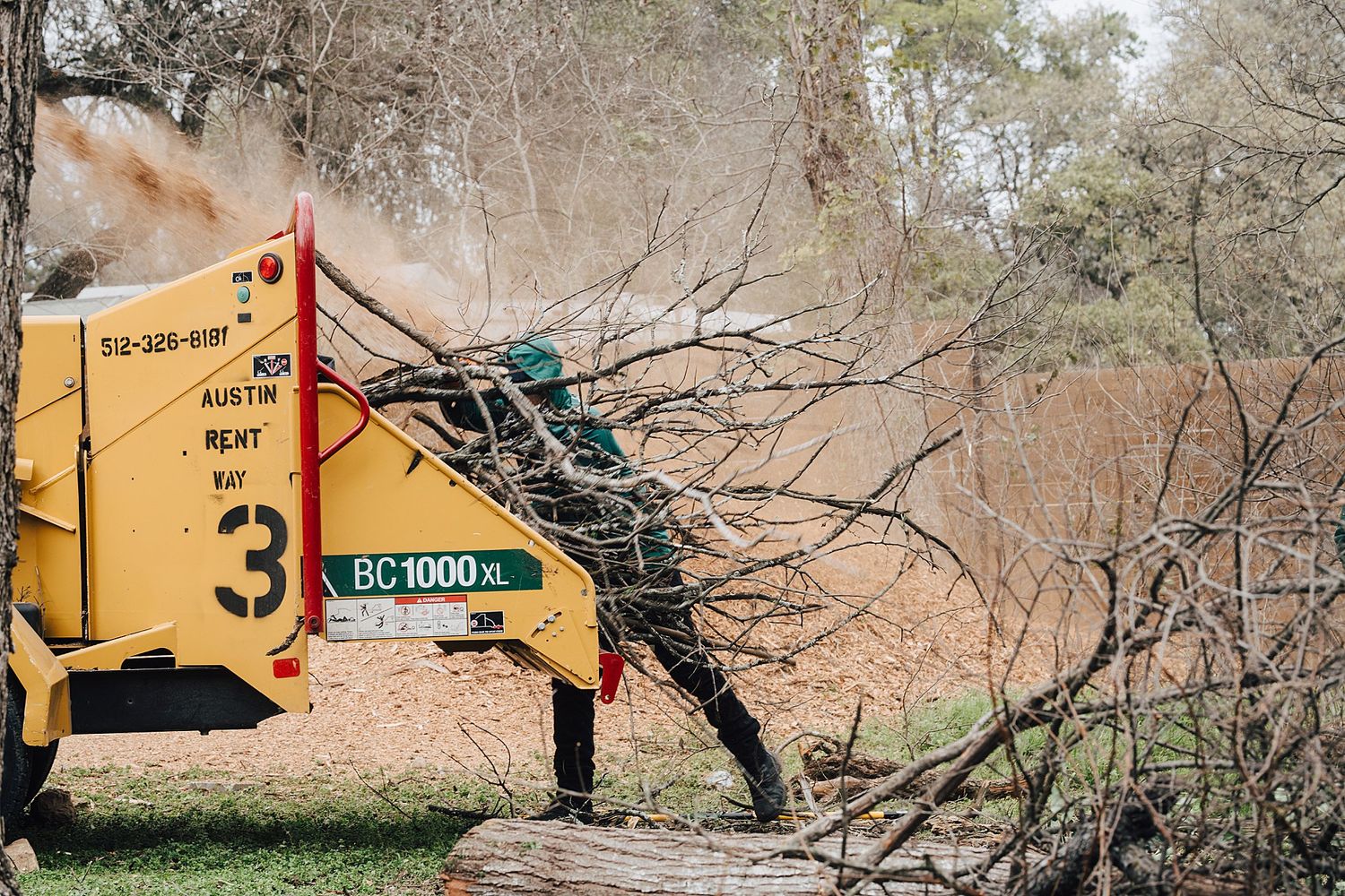Industrial wood chipper machine processing tree branches in a wooded area.