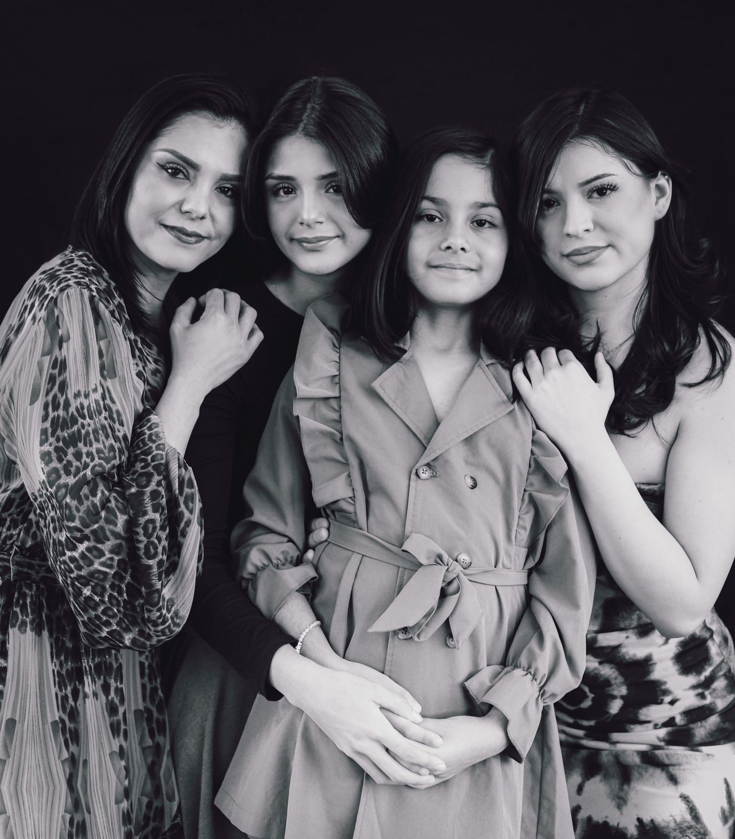 Group portrait of four women in stylish outfits against black backdrop.