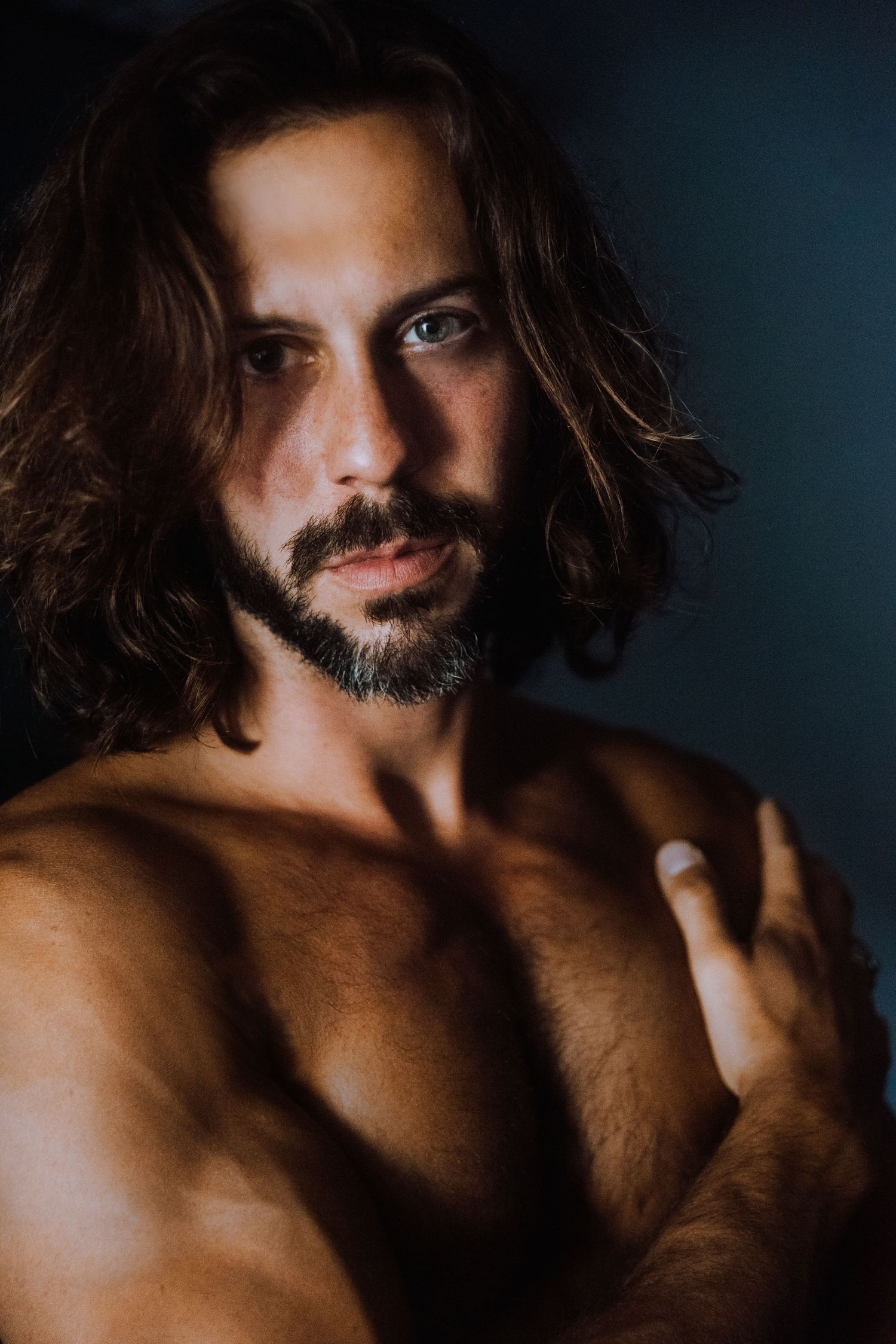Dramatic close-up portrait of long-haired person with beard in dark moody lighting.