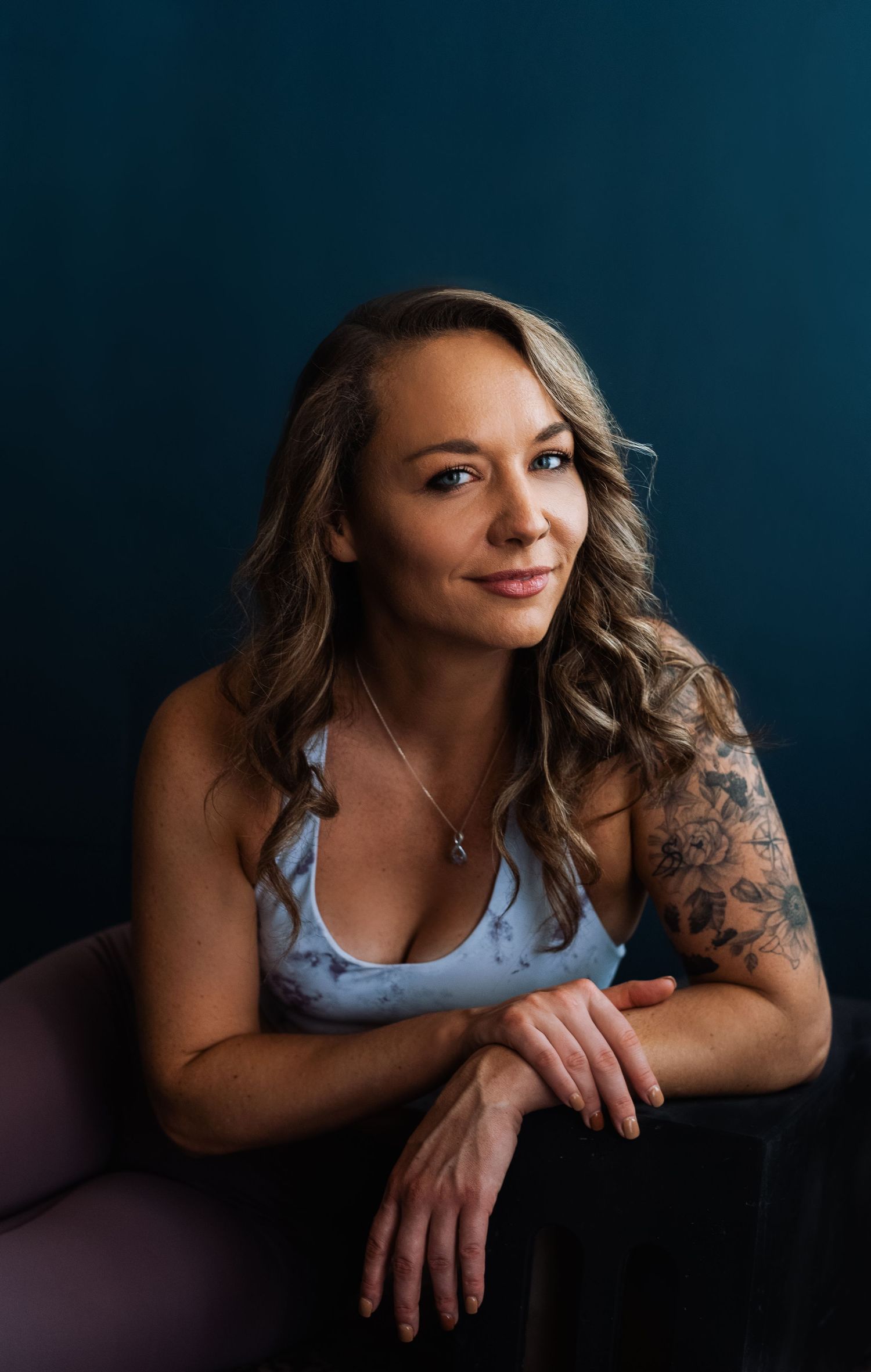 Portrait showing a relaxed pose against a dark background with wavy hair and a tank top.