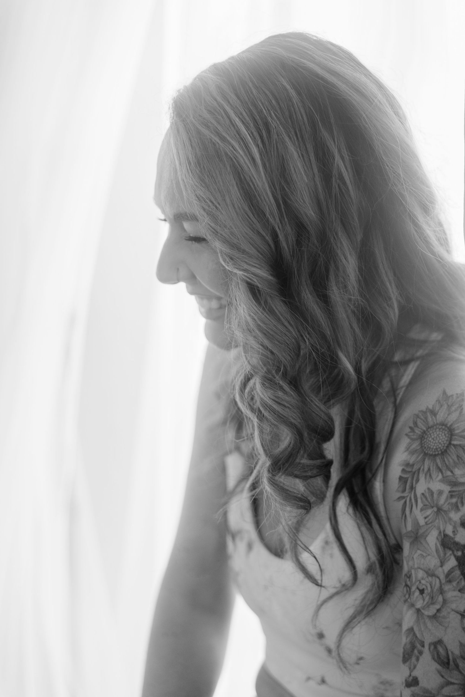 Black and white profile portrait showing long wavy hair and floral tattoo artwork.