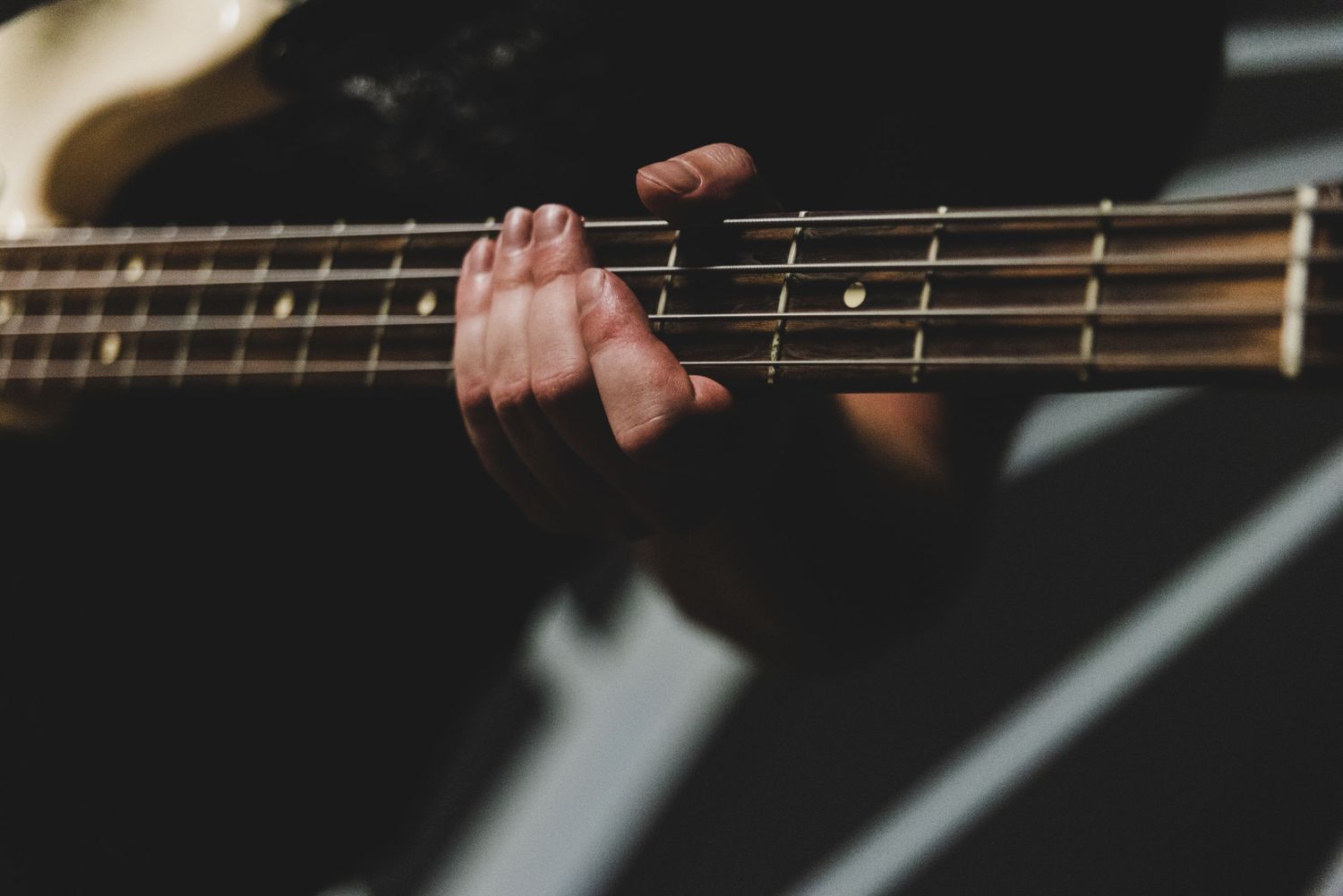 Close-up of hand playing bass guitar strings against dark background.