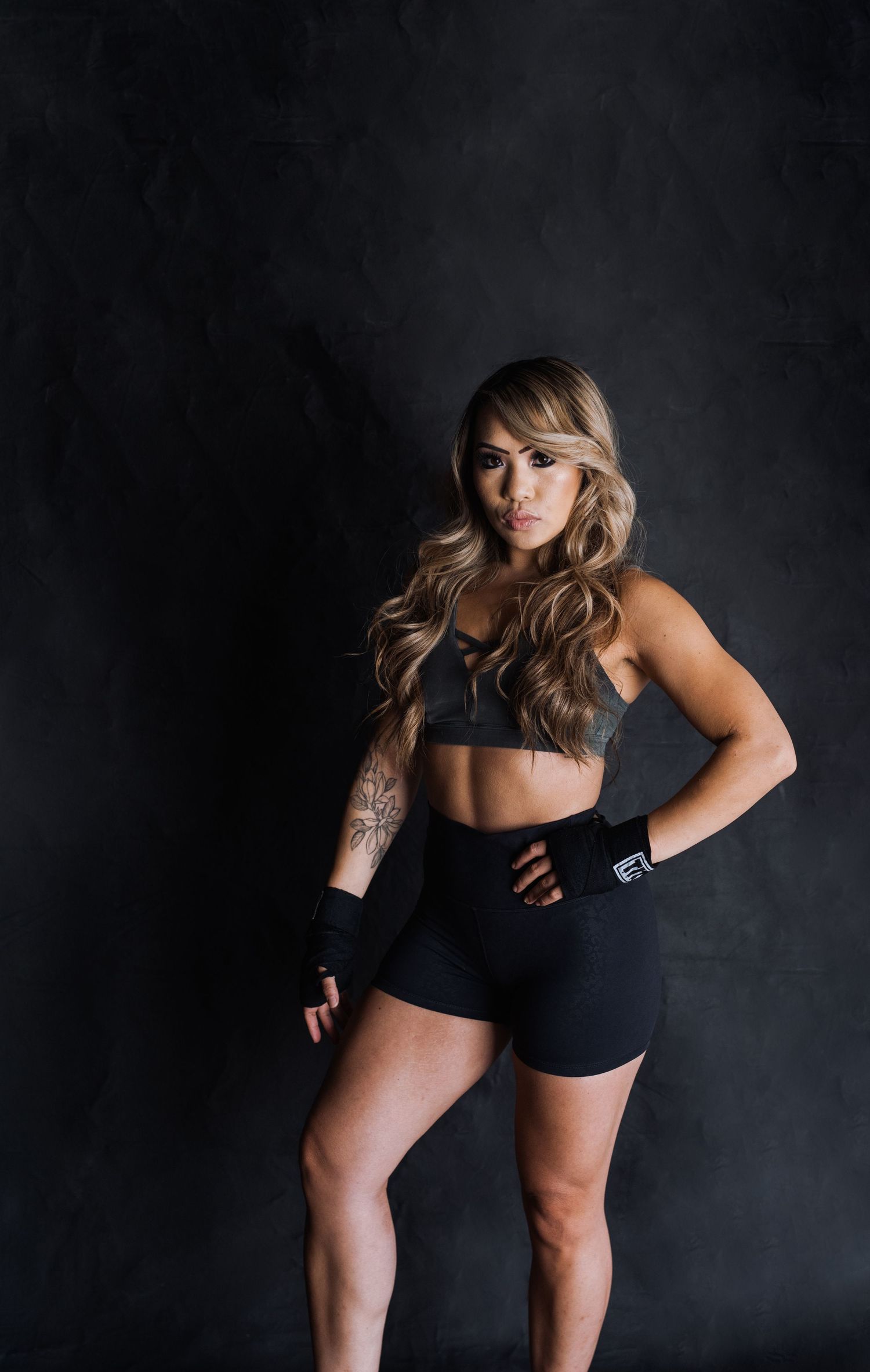 Athletic woman in black workout attire poses confidently against dark background.