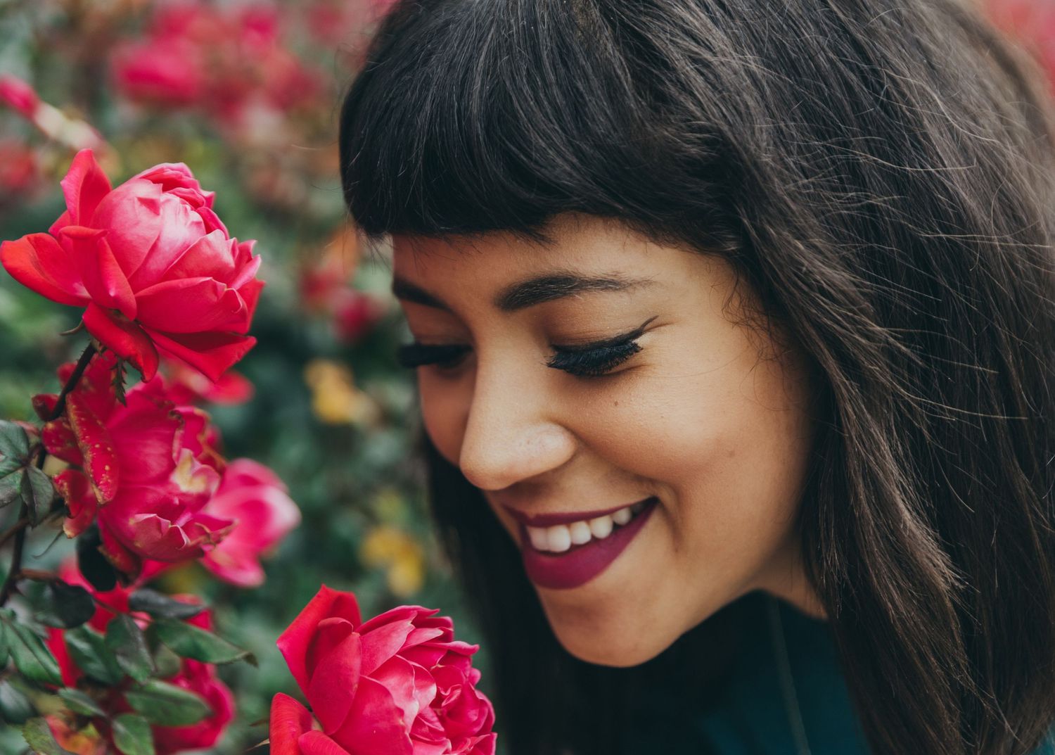 Close-up of person smiling near vibrant red roses in garden setting.
