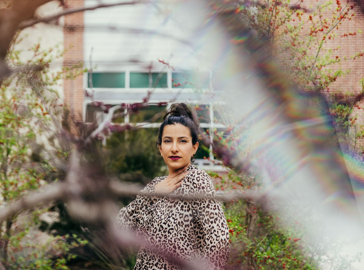 Person in leopard print dress photographed through blossoming tree branches with soft focus effect.