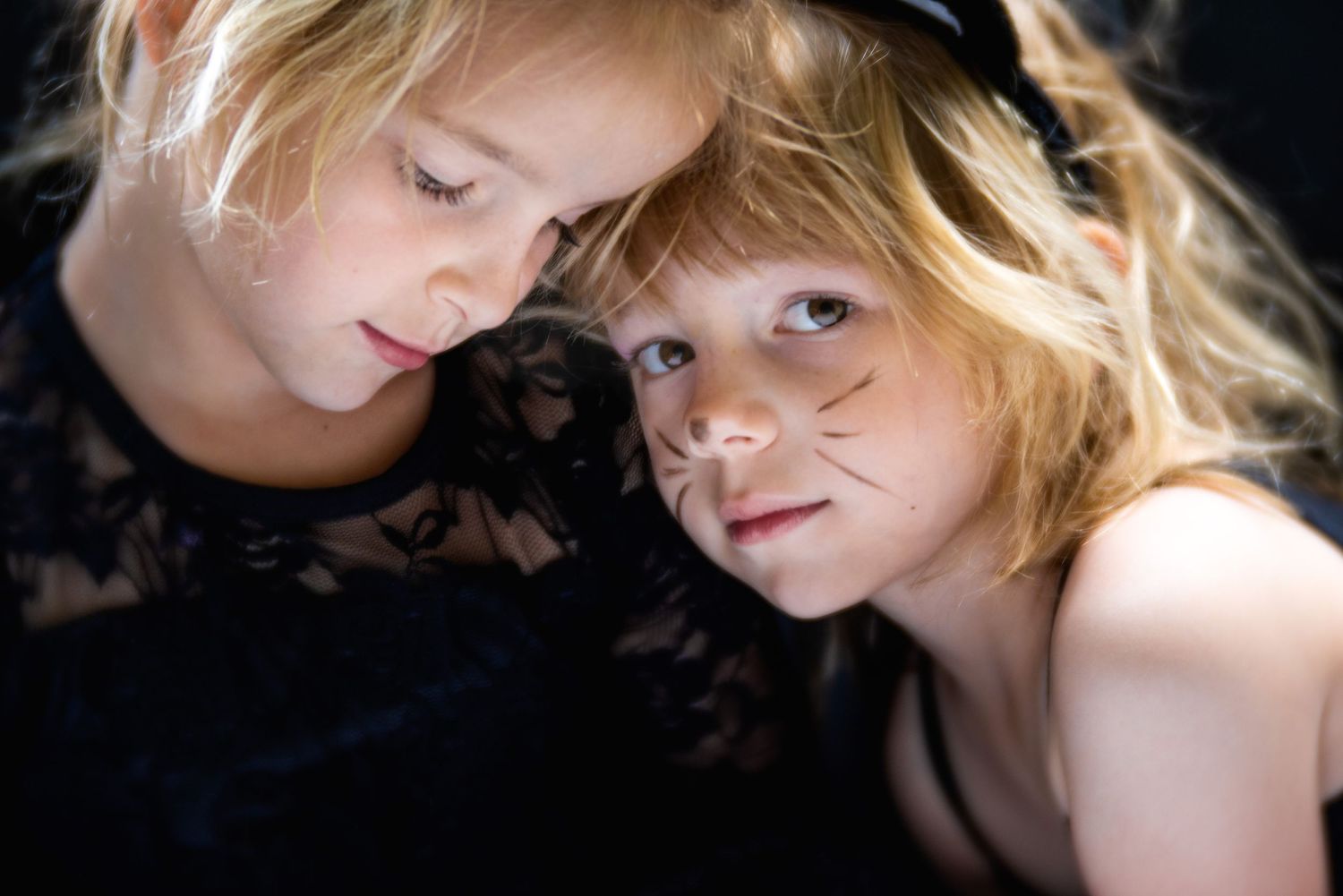 Artistic portrait of two children with blonde hair against dark background.