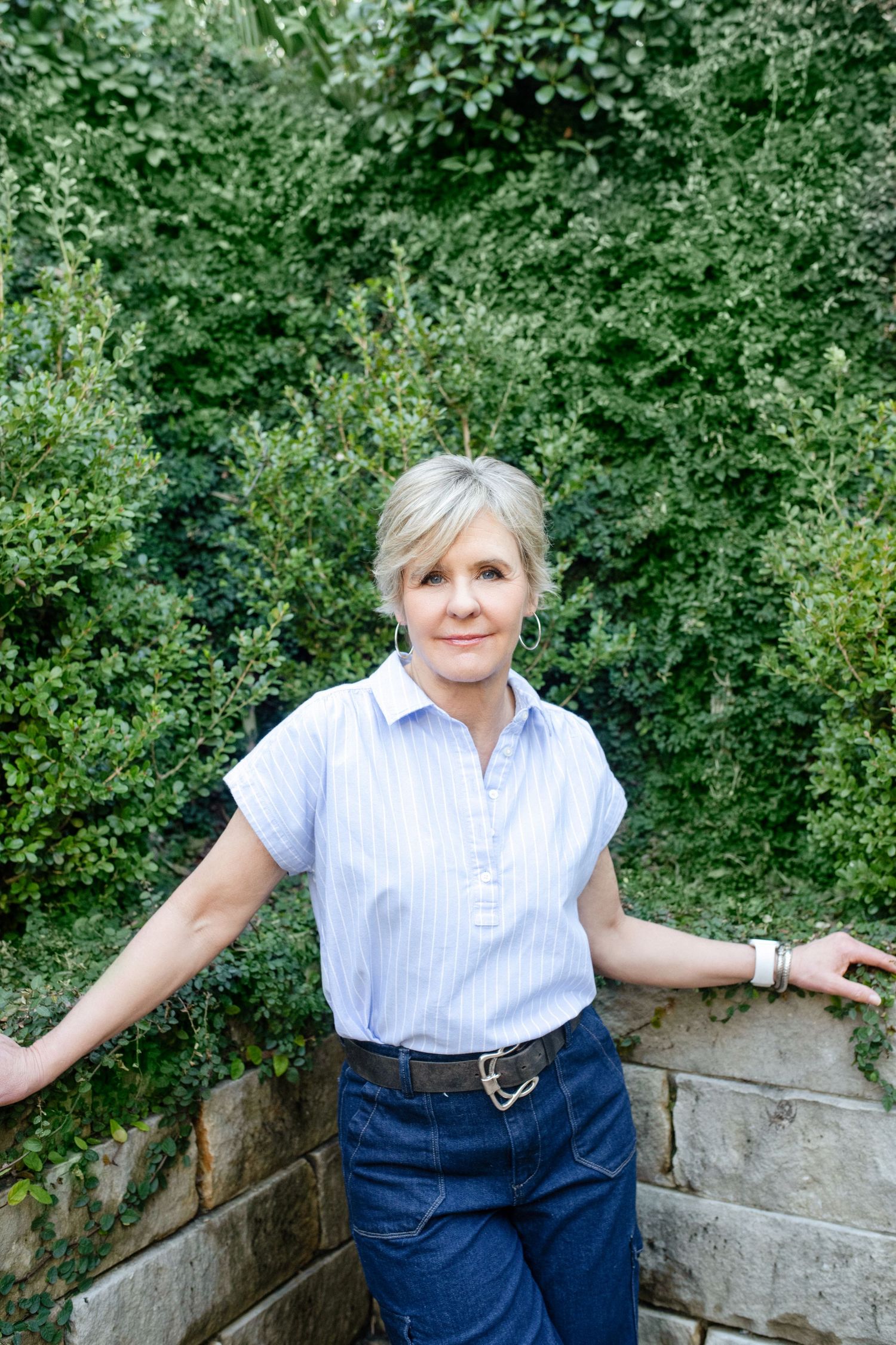 A casual summer outfit with a striped button-down shirt and jeans styled in an outdoor garden setting.
