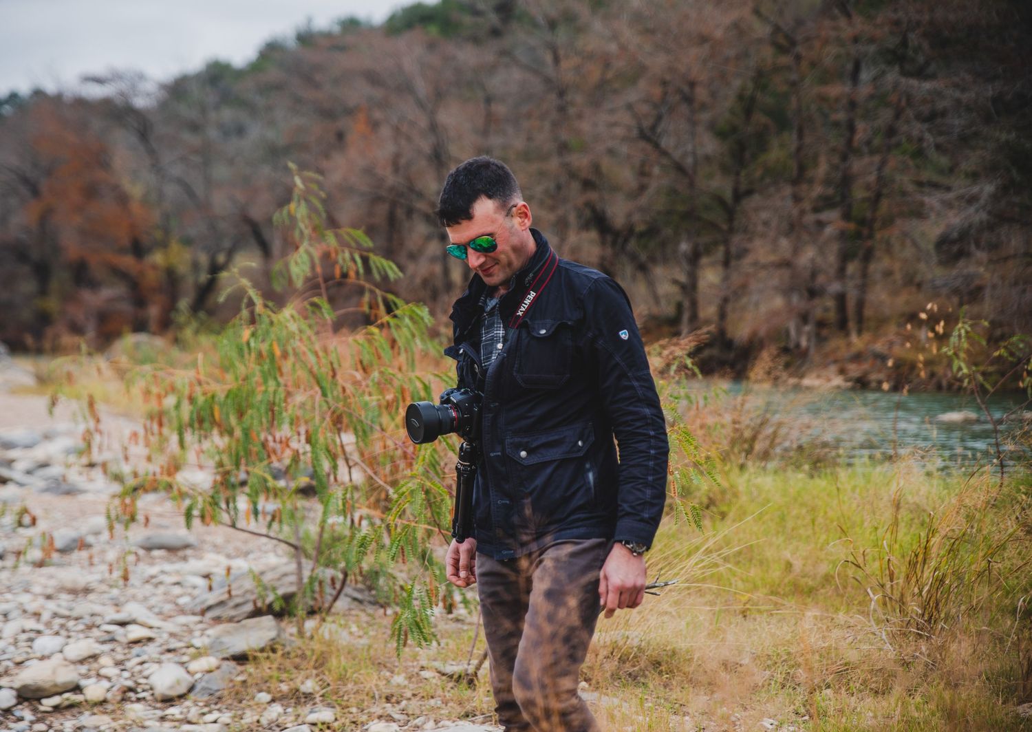 Person hiking on rocky trail wearing dark jacket in autumn landscape.