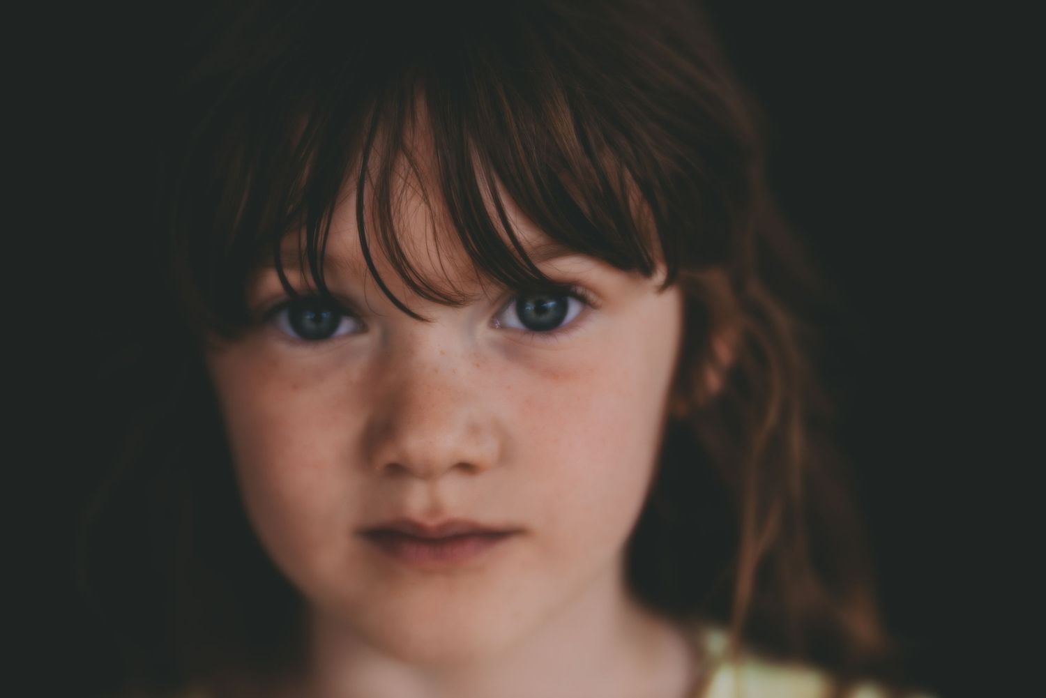 Dramatic close-up portrait of young child with bangs in dark lighting.