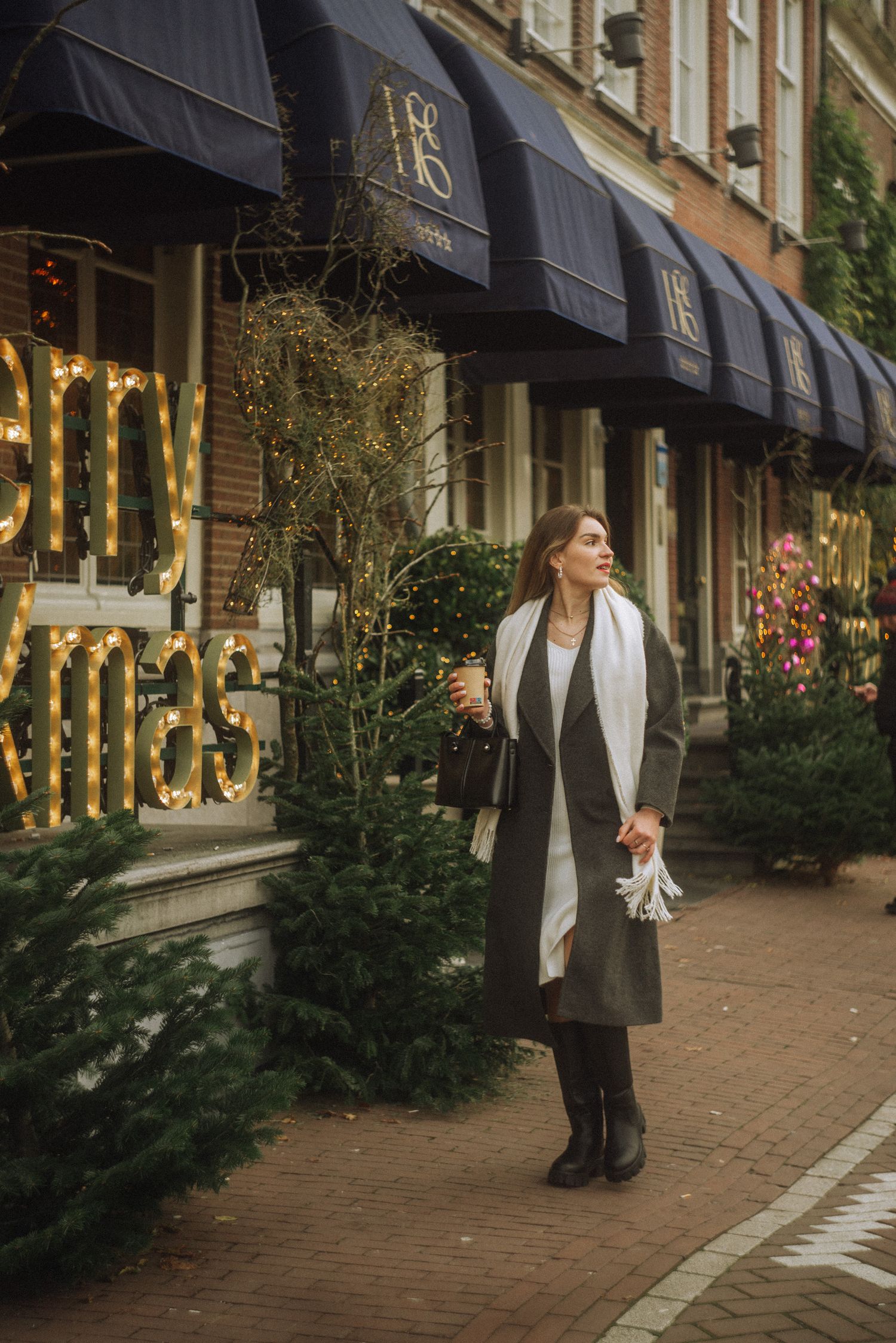 Christmas trees line a cobblestone street with storefronts decorated for the holidays.