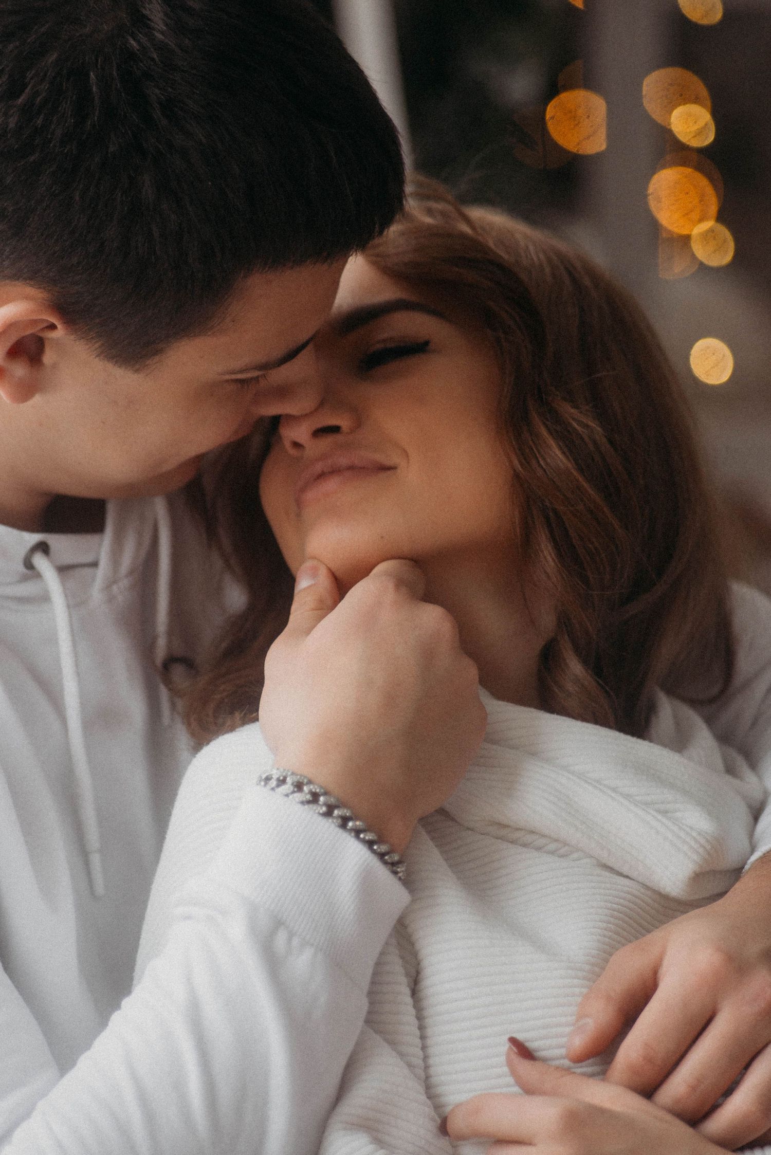 Intimate moment captured in warm lighting with festive bokeh in background.