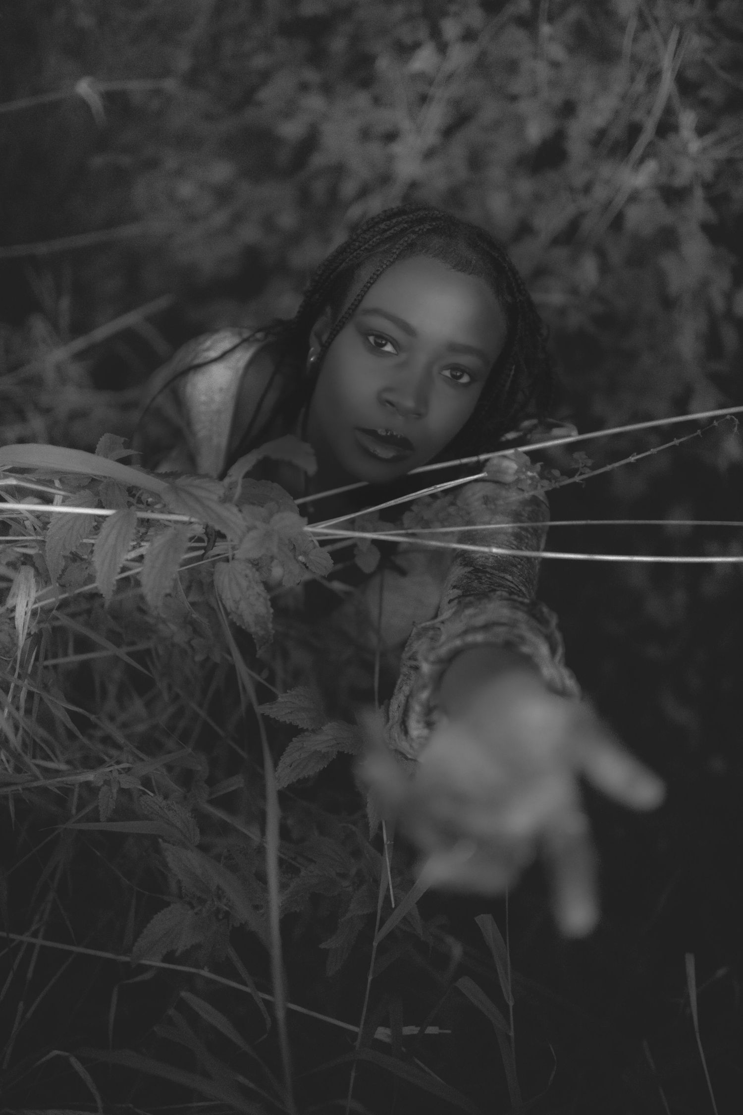 Artistic black and white portrait with reaching hand through foliage.