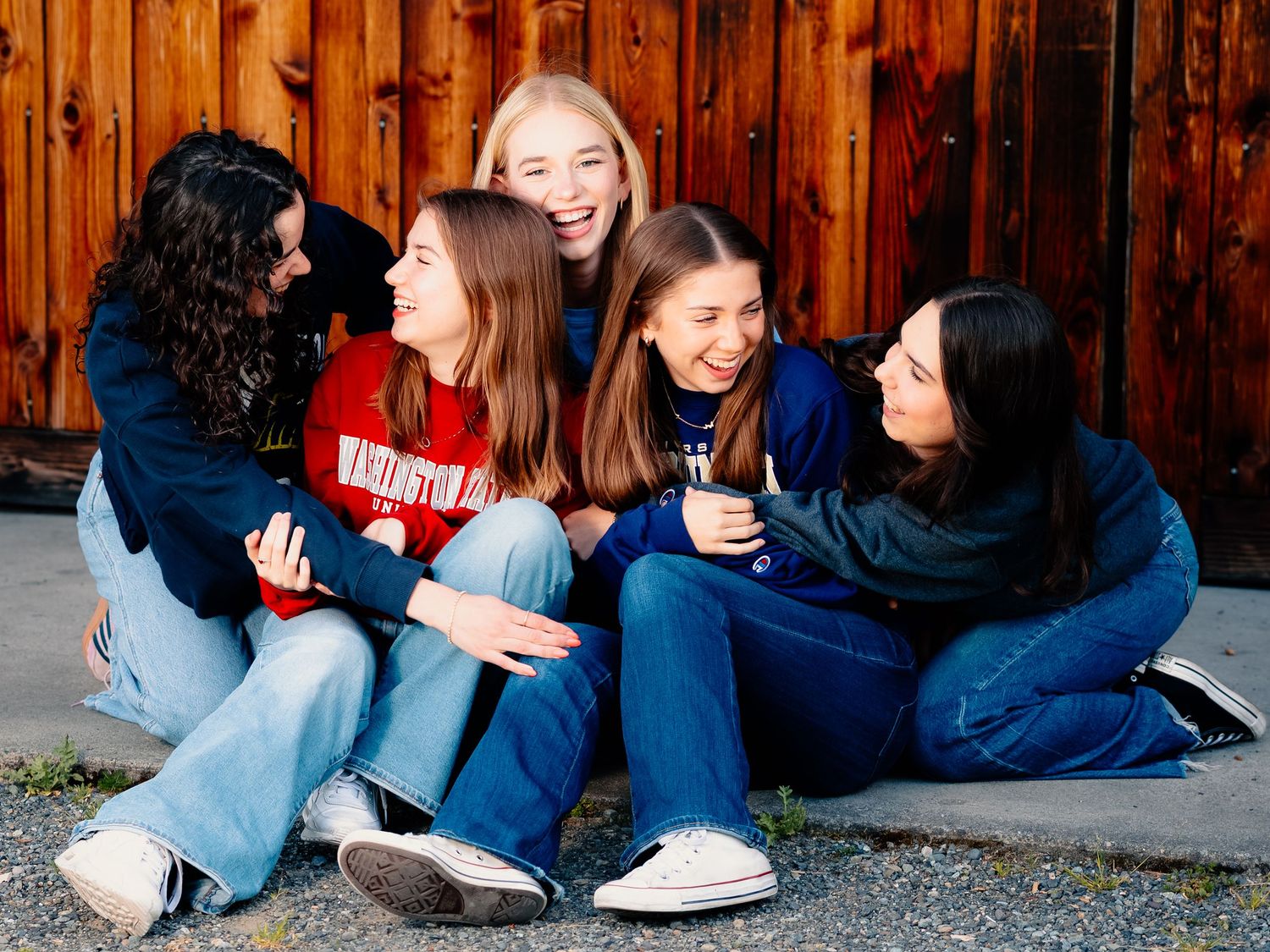 Group of teenagers sitting casually against a wooden fence sharing relaxed conversation and laughter.