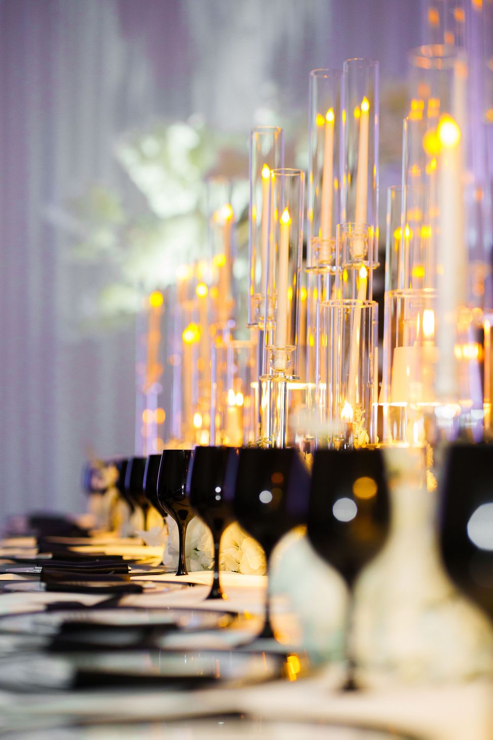 Elegant banquet table with black wine glasses, glowing candles, and tall glass centerpieces at a formal event.