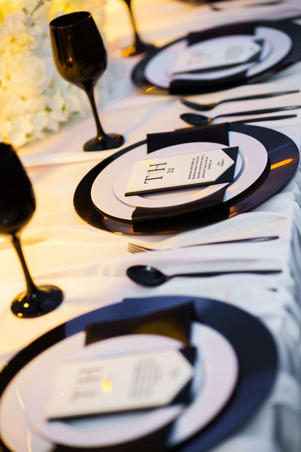 Elegant black and white wedding table setting with monogrammed menus, black stemware, and white floral centerpieces.