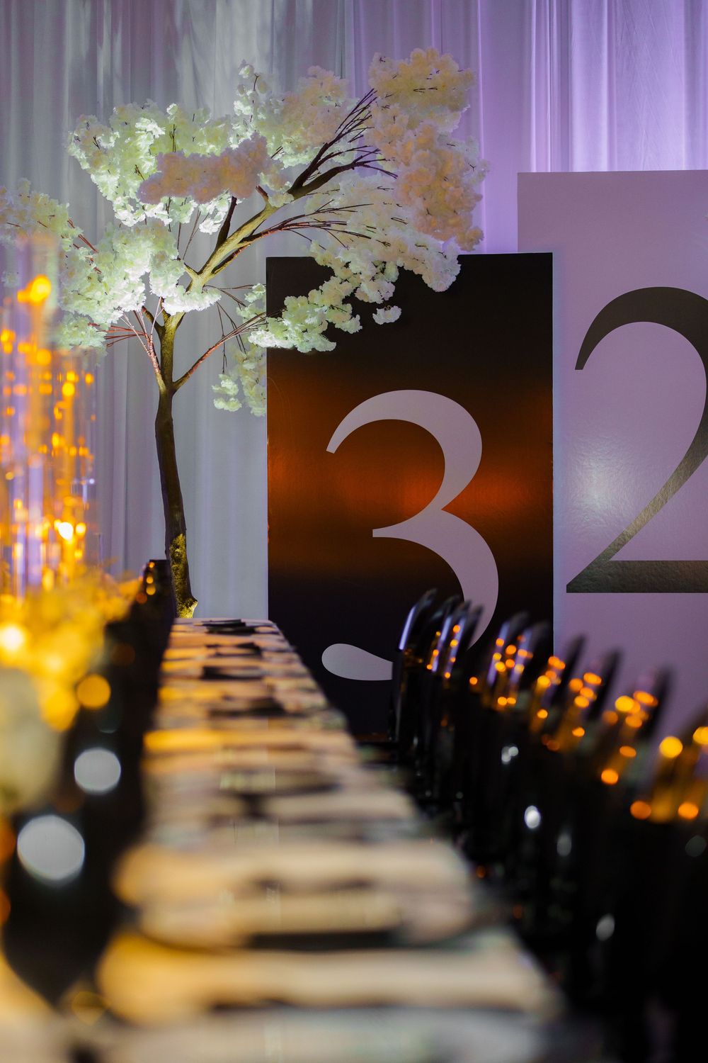 Elegant wedding reception table with cherry blossom centerpiece, glowing candles, and numbered table signs 3 and 2.