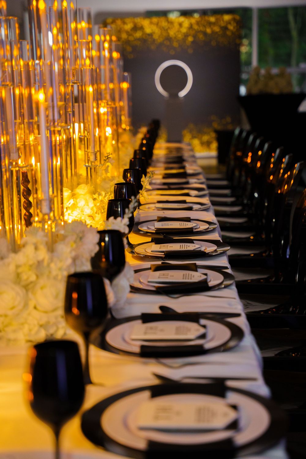 Elegant black and gold wedding reception table setting with glowing candelabras, white floral arrangements, and black charger plates.