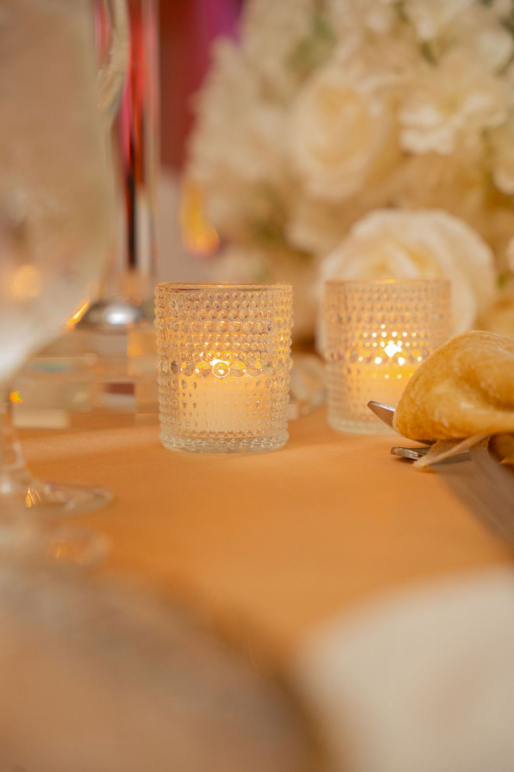 Elegant wedding table setting with glowing crystal votive candles, white roses, and soft peach linen.