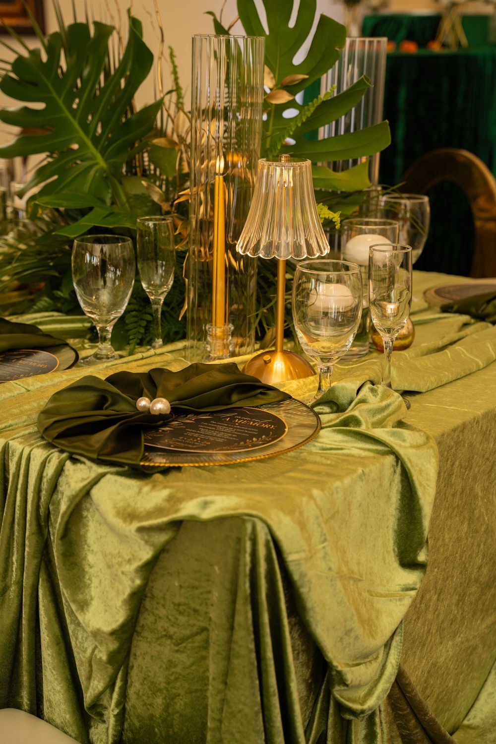 Elegant green velvet table setting with gold candelabra, crystal glasses, and tropical monstera leaves for a luxury event.