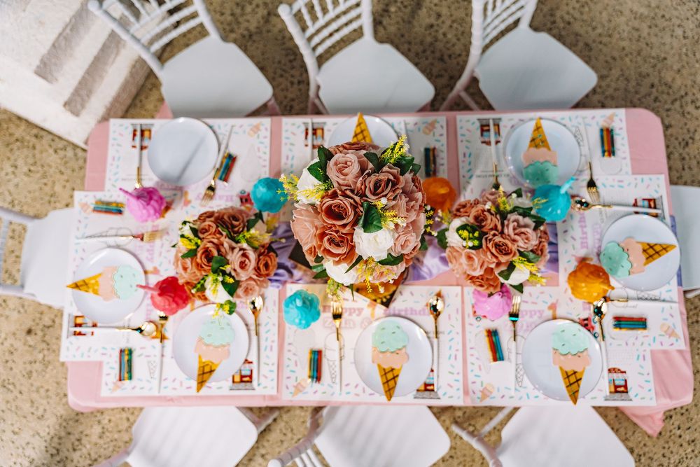 Colorful party table setup with pink tablecloth, floral centerpiece, ice cream cone plates, and balloon decorations viewed from above.