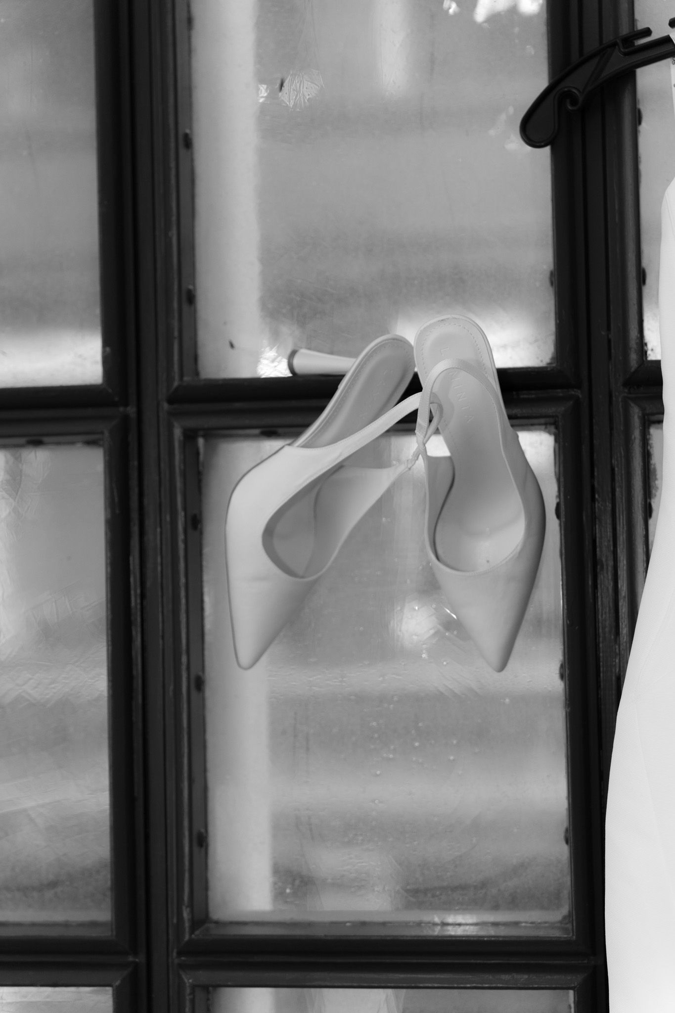 Black and white photo of elegant white high heels displayed in a window frame.