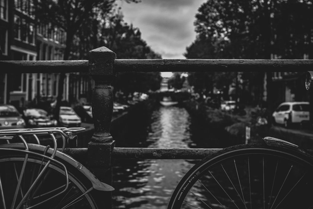 Svartvit bild av en kanal i Amsterdam med bro och cyklar