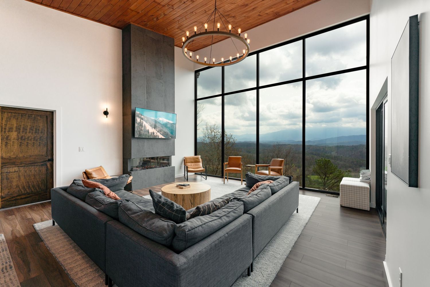 Contemporary living room with sectional sofa, fireplace, and floor-to-ceiling windows showcasing mountain vistas.