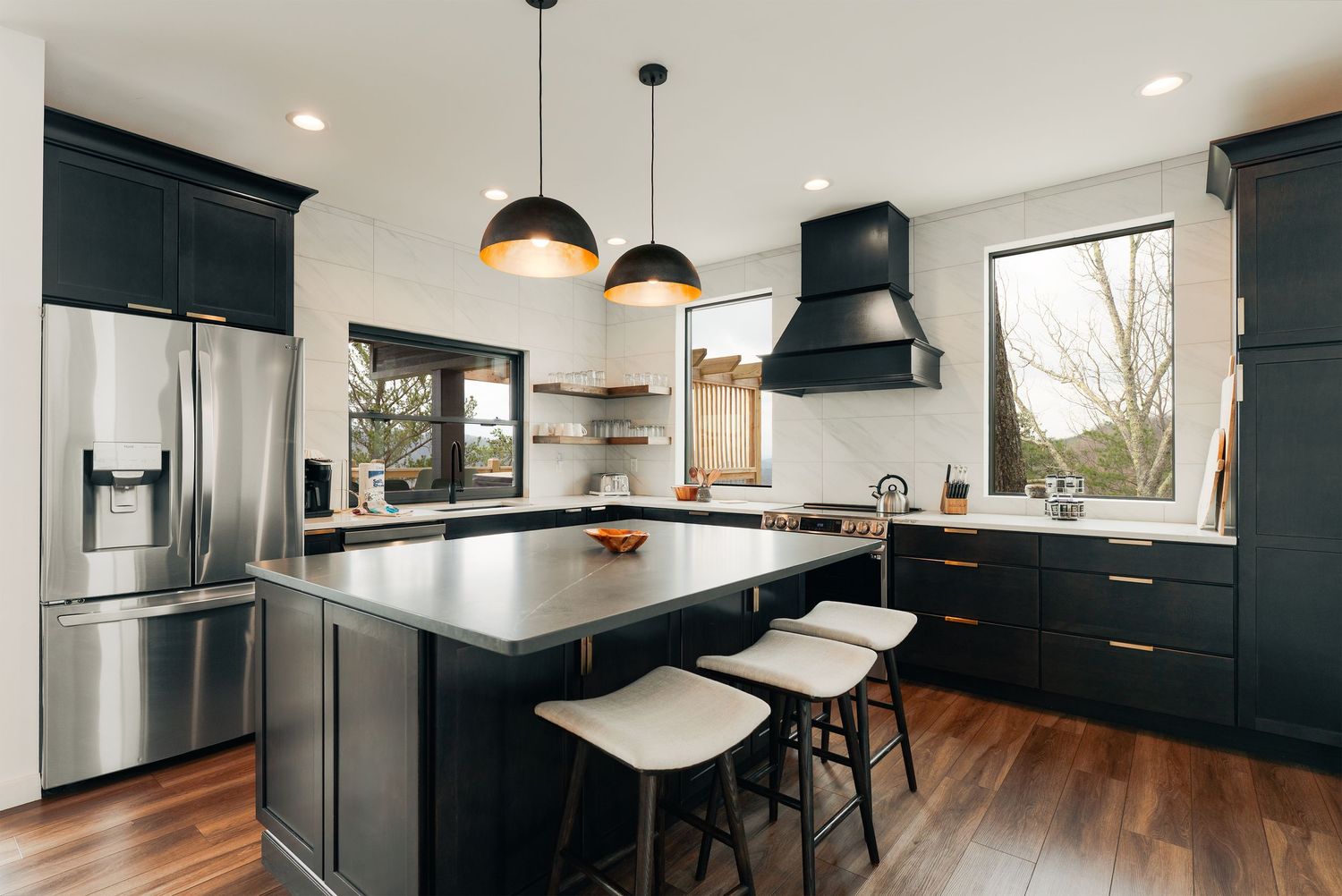 Modern kitchen with dark navy cabinets, stainless appliances, pendant lights and white waterfall countertop island.