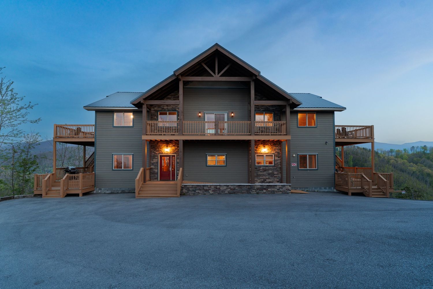 Large modern mountain cabin with dual balconies and dark exterior illuminated at dusk.