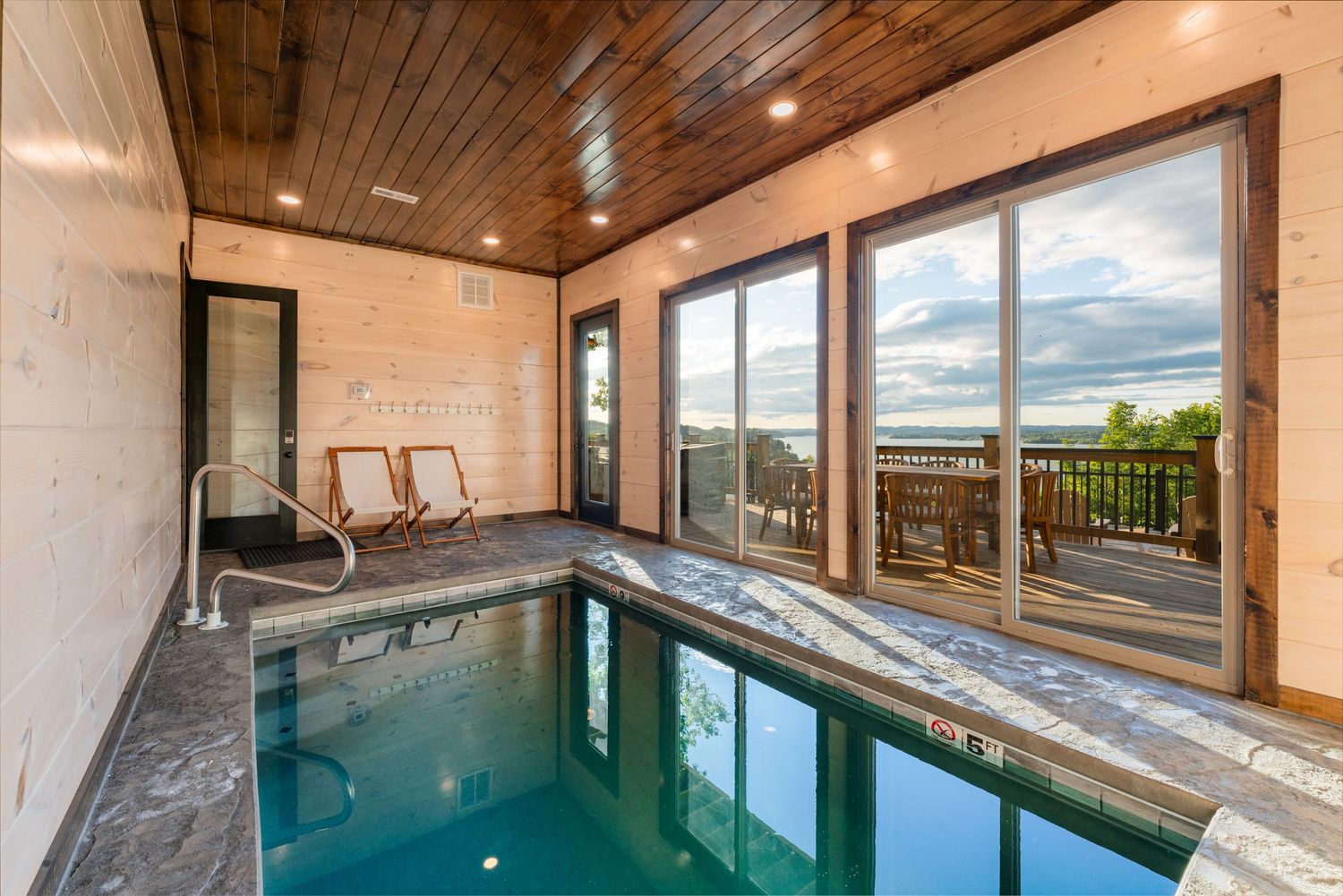 Indoor swimming pool with wooden ceiling and large sliding doors opening to mountain views.