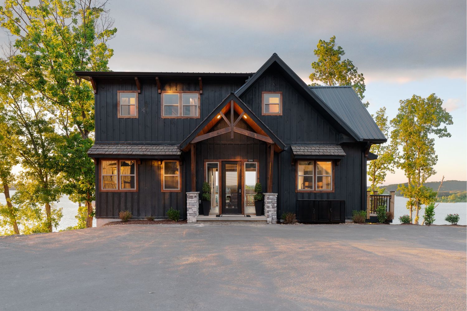 Modern black lake house with rustic timber accents and large windows overlooking the water at dusk.