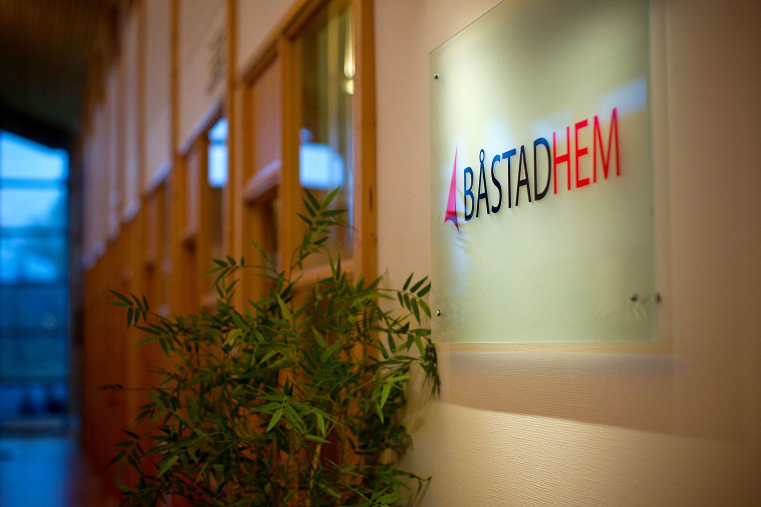 An office interior showing a Bastadhem company sign mounted on a wall with a decorative plant in the foreground.