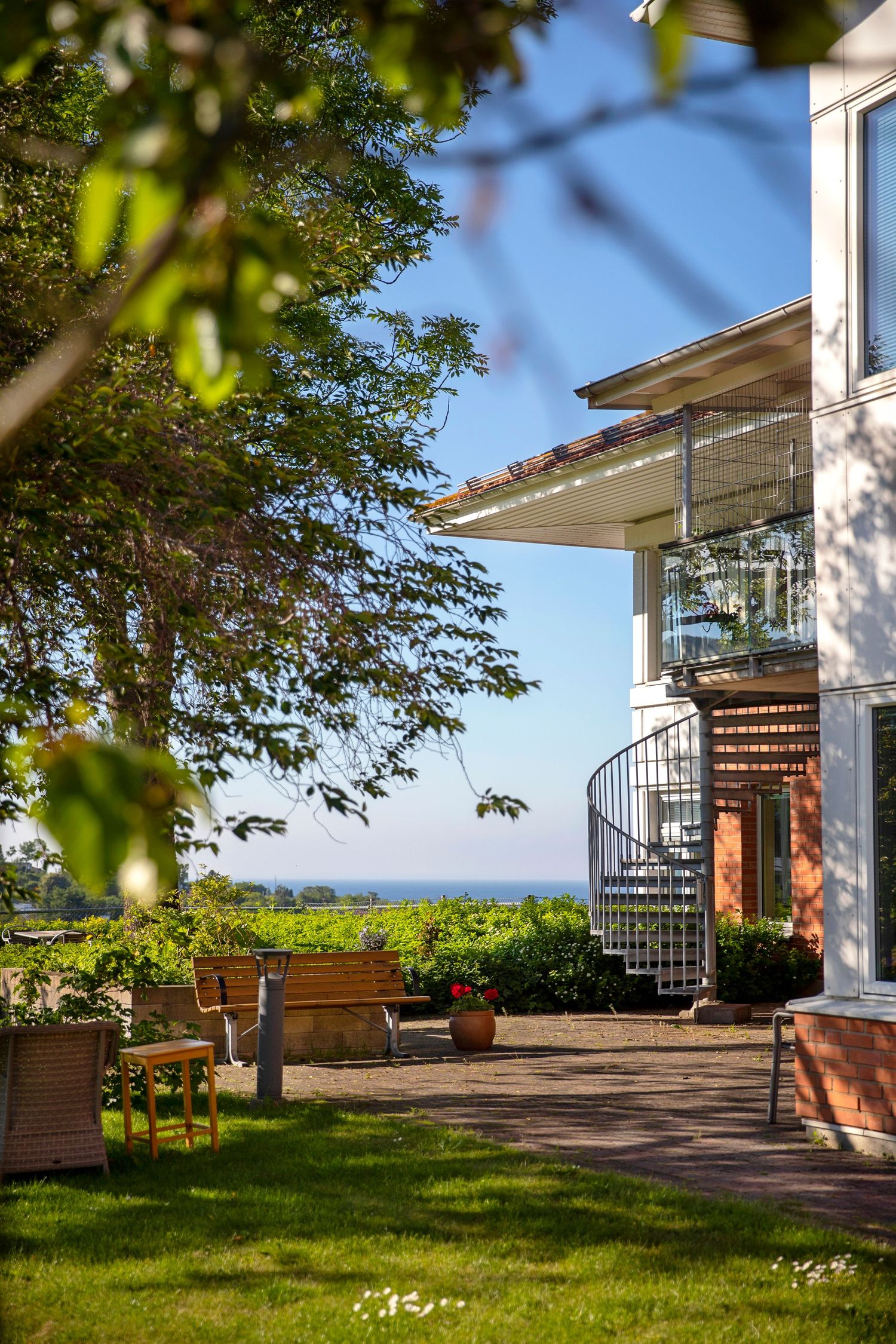 Panoramic view of a modern white house terrace with spiral staircase and lush garden overlooking scenic landscape.