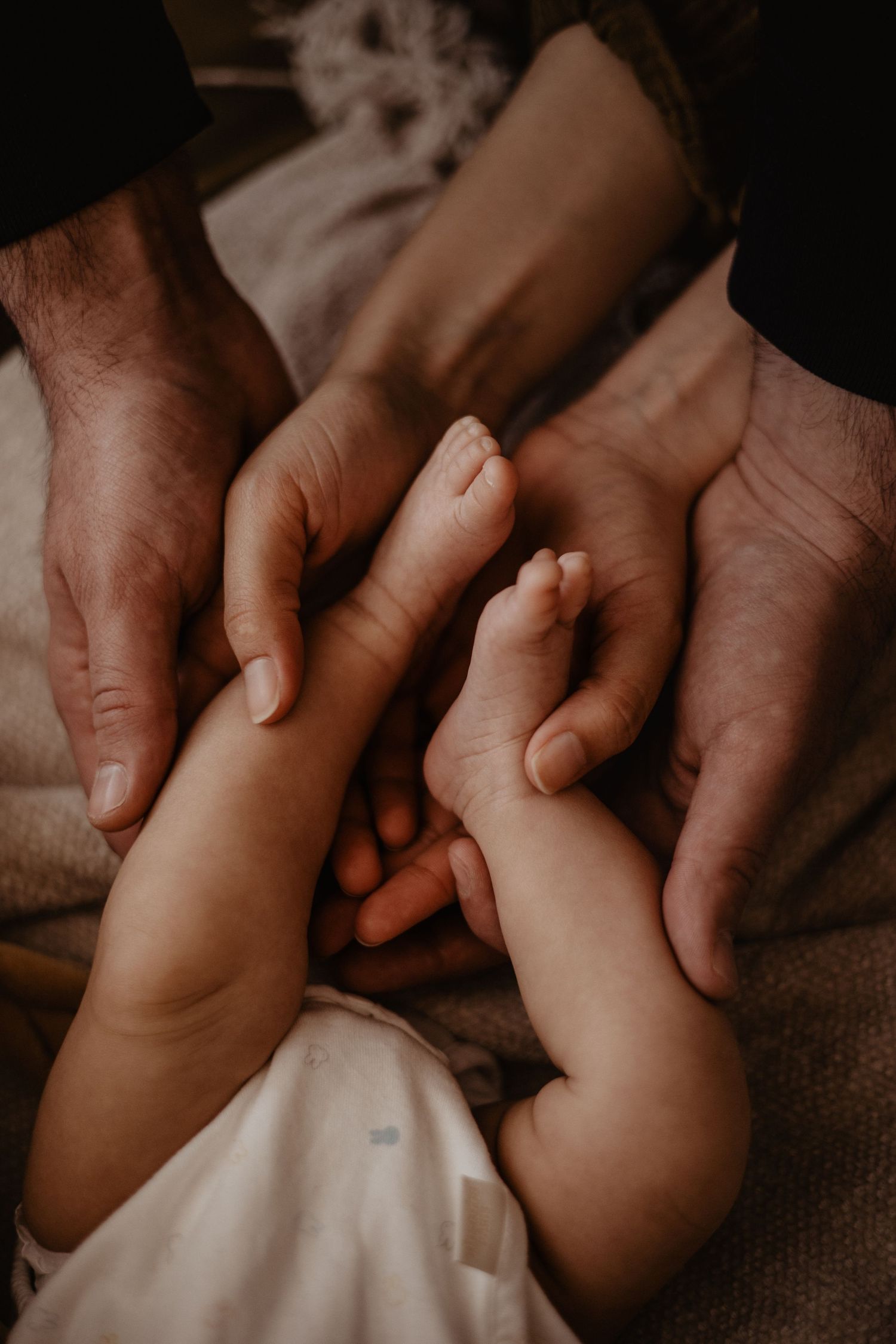 Photo de pieds d'un nouveau né dans les mains de ses deux parents lors d'une séance naissance