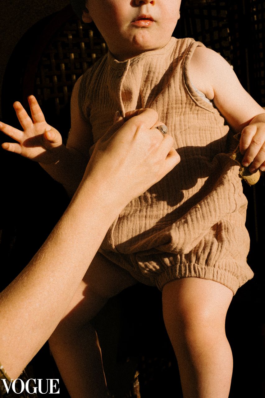 A close-up shot of a child in beige romper with reaching hands in warm vintage lighting.