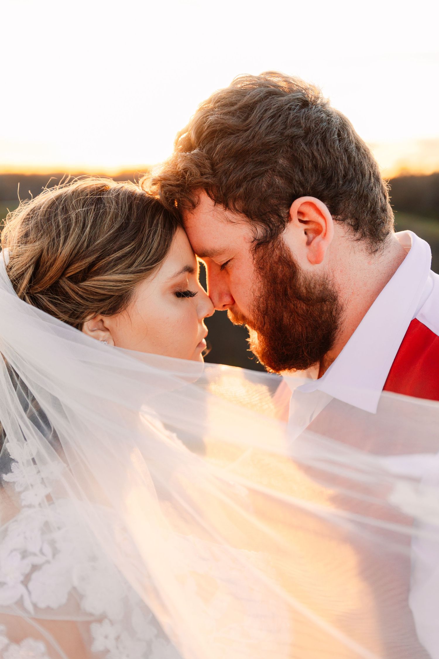 Romantic sunset wedding photos with flowing veil creating ethereal lighting effect.