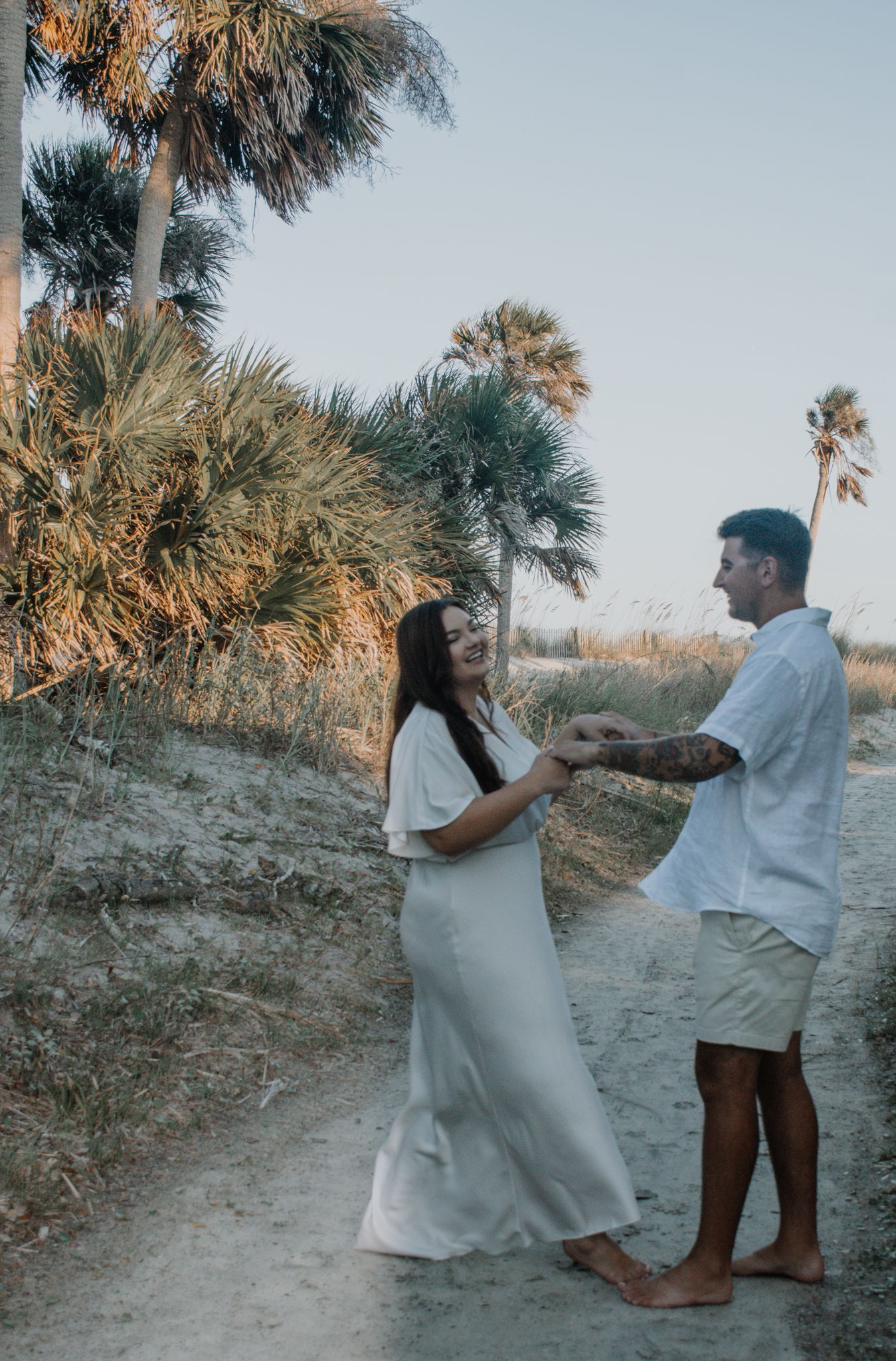 A couple sharing a tender moment on a sandy trail surrounded by tropical vegetation.