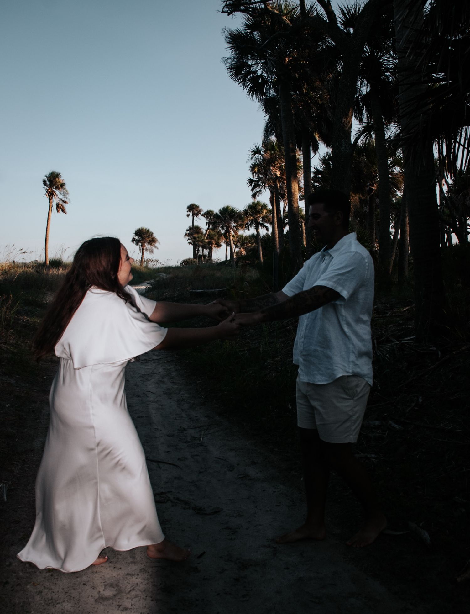 A playful moment between a couple on a beach path with palm trees in the background.