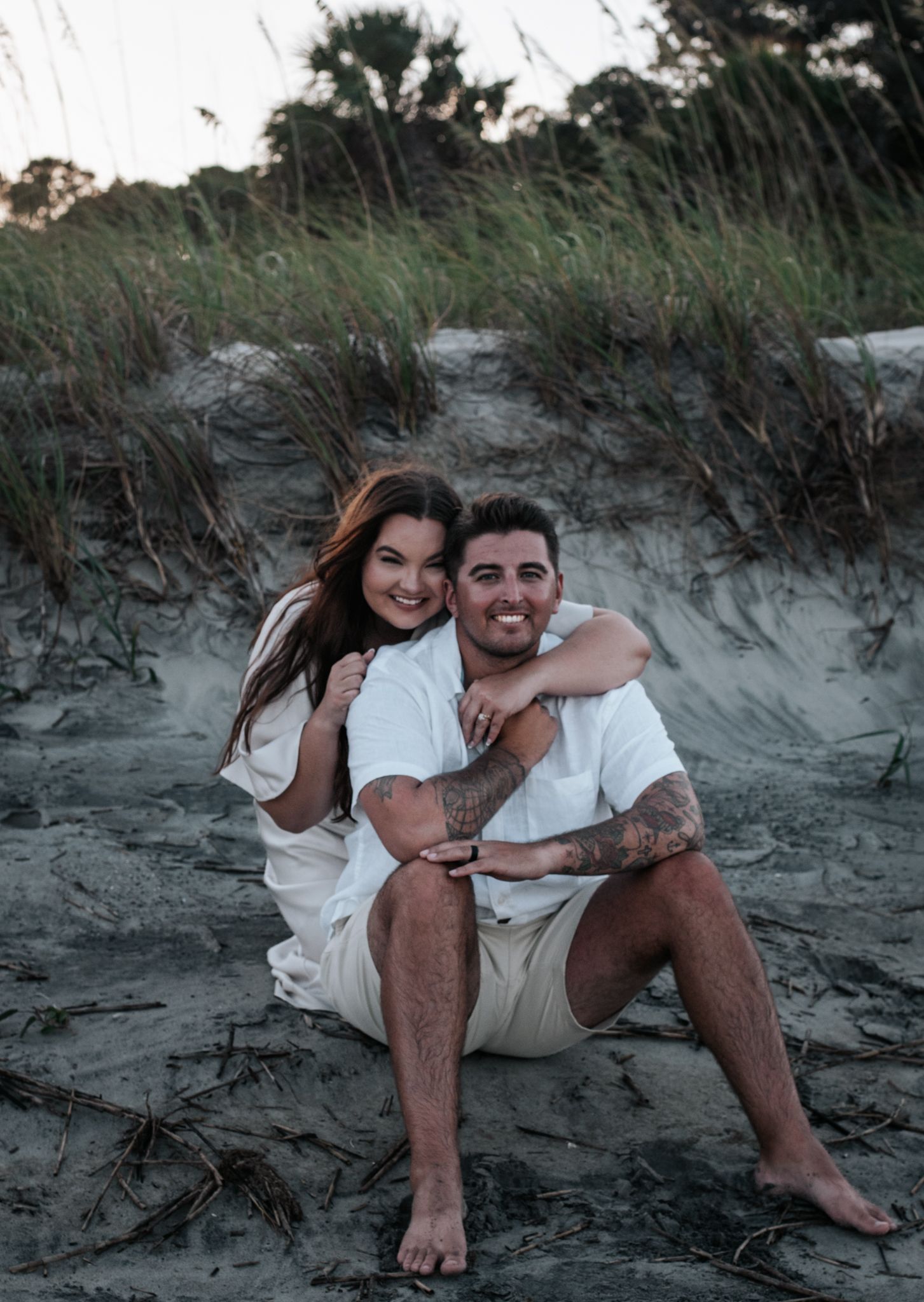 A couple in white outfits sharing a joyful moment on sandy dunes.